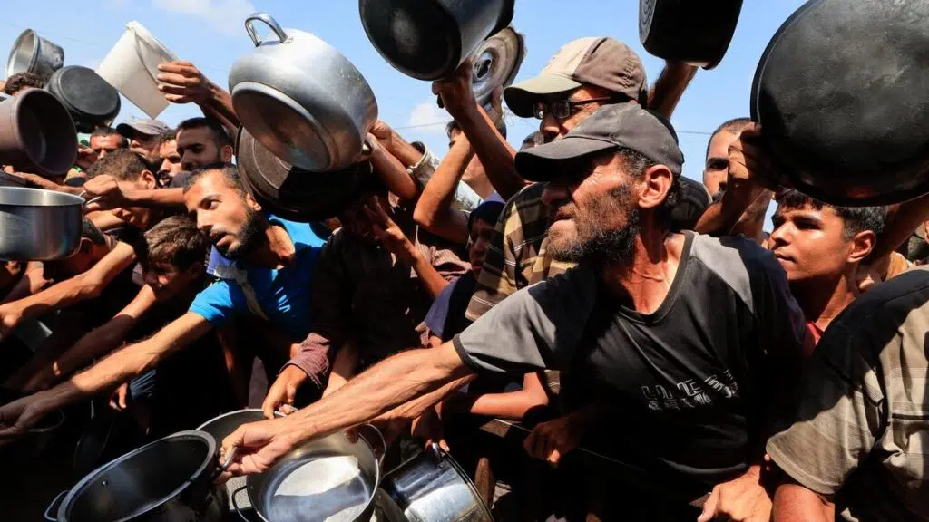 Palestinians reach out with pots and containers while waiting to receive food from a charity kitchen in Khan Younis, southern Gaza Strip,