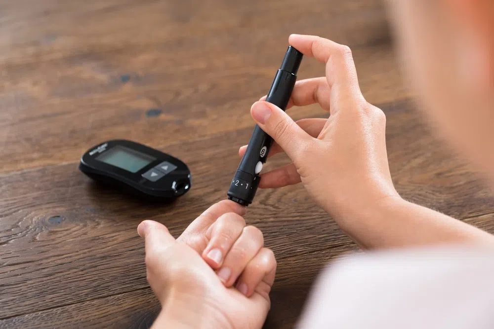 Person performing fingerstick blood glucose test using a lancet device and glucose meter for daily diabetes monitoring